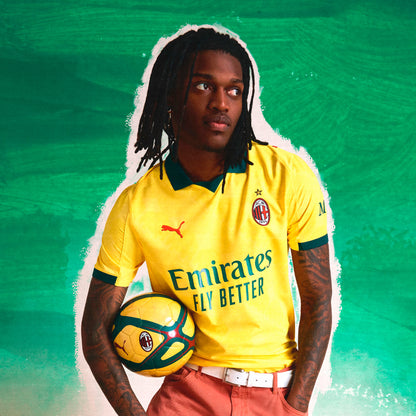 Person wearing a yellow sports jersey with visible branding, holding a soccer ball against a green background