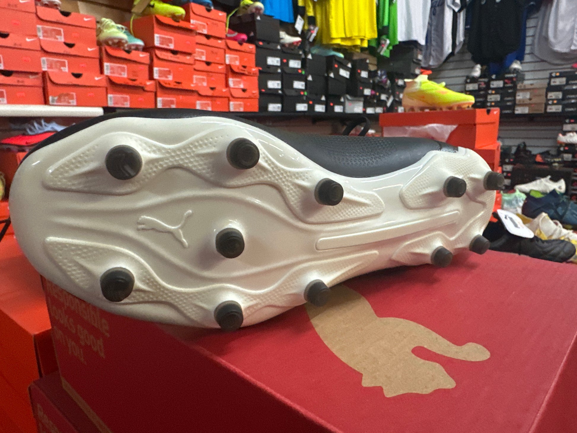 White soccer cleat with black studs on a red display box in a store setting