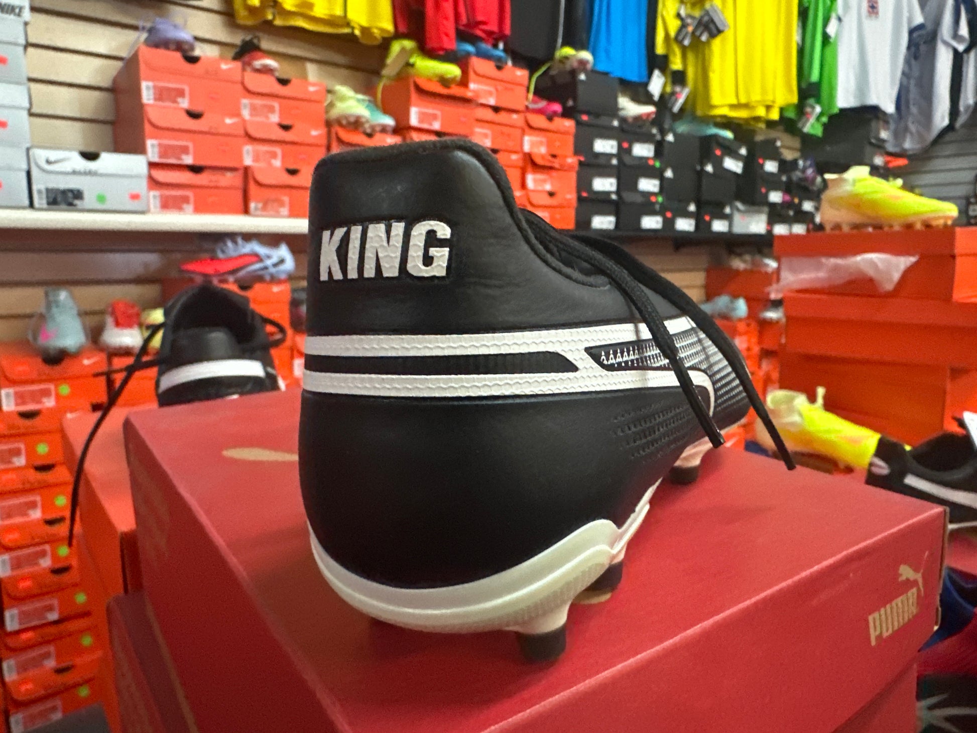 Black sports shoe with 'KING' branding on a red box in a store setting.