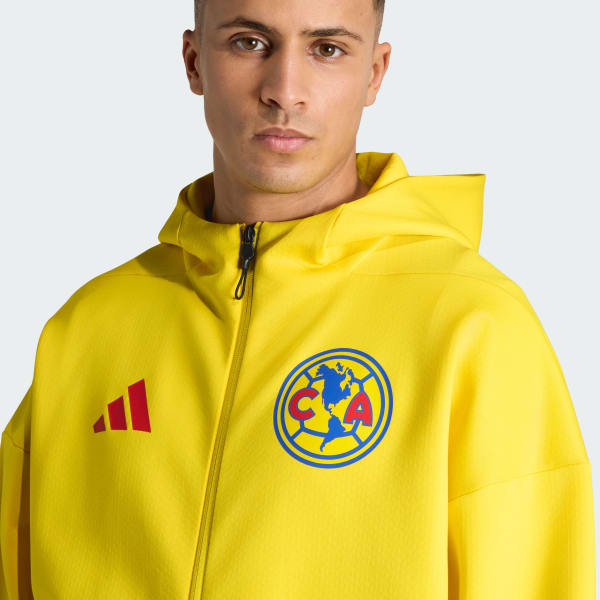 Man wearing a yellow jacket with Adidas and Club América logos on a light gray background
