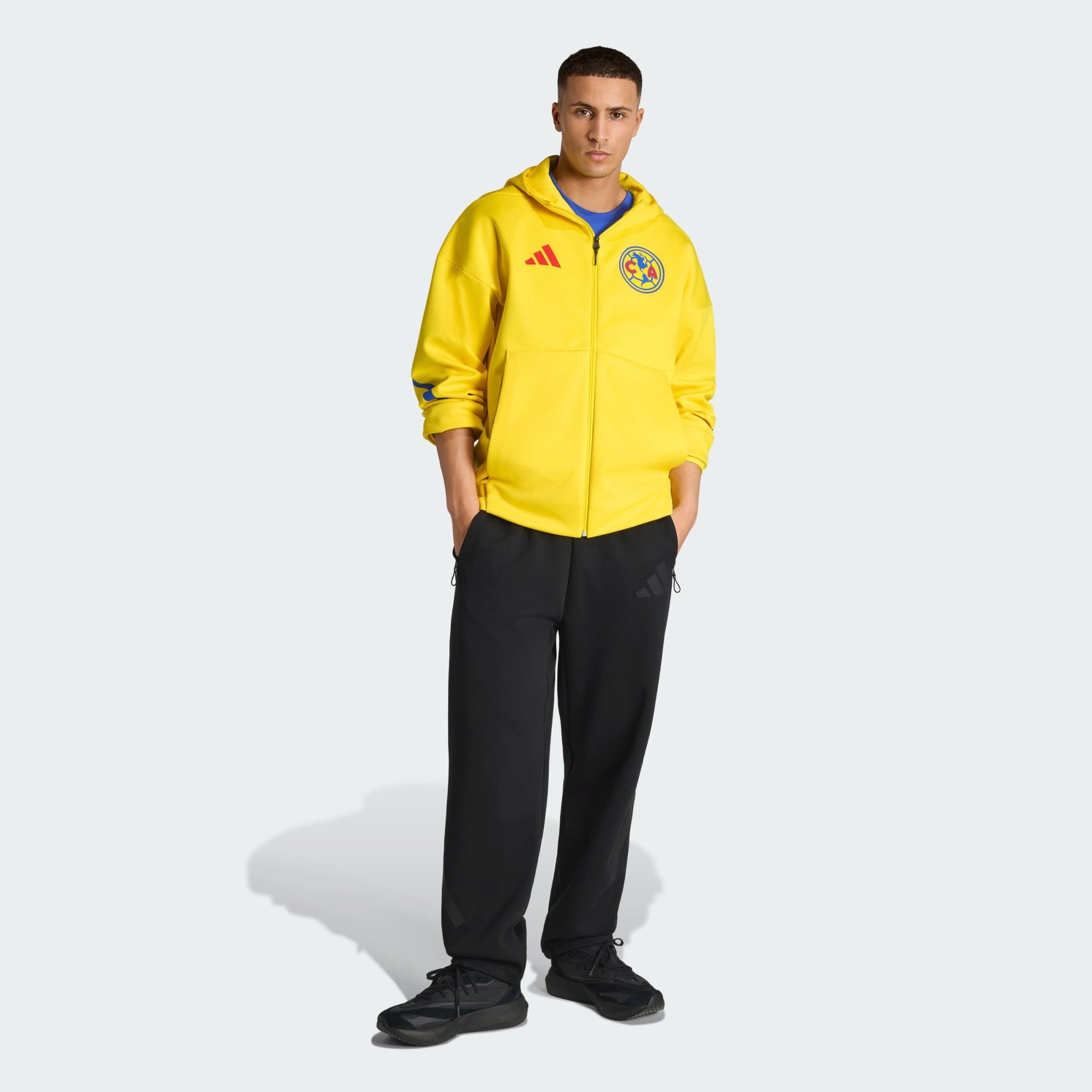 Person wearing a yellow Adidas tracksuit with a logo on a white background