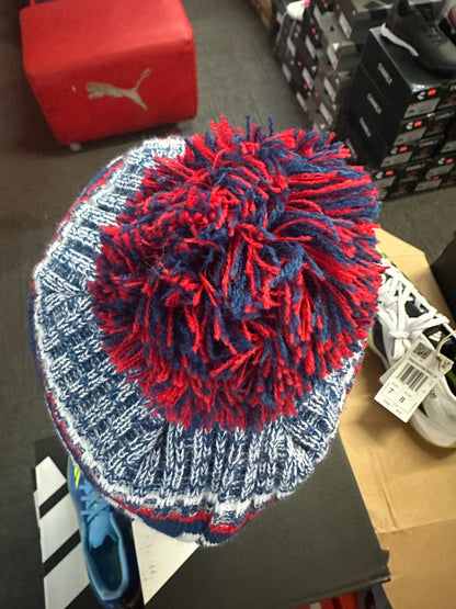 Knitted beanie with red and blue pom-pom on a black surface
