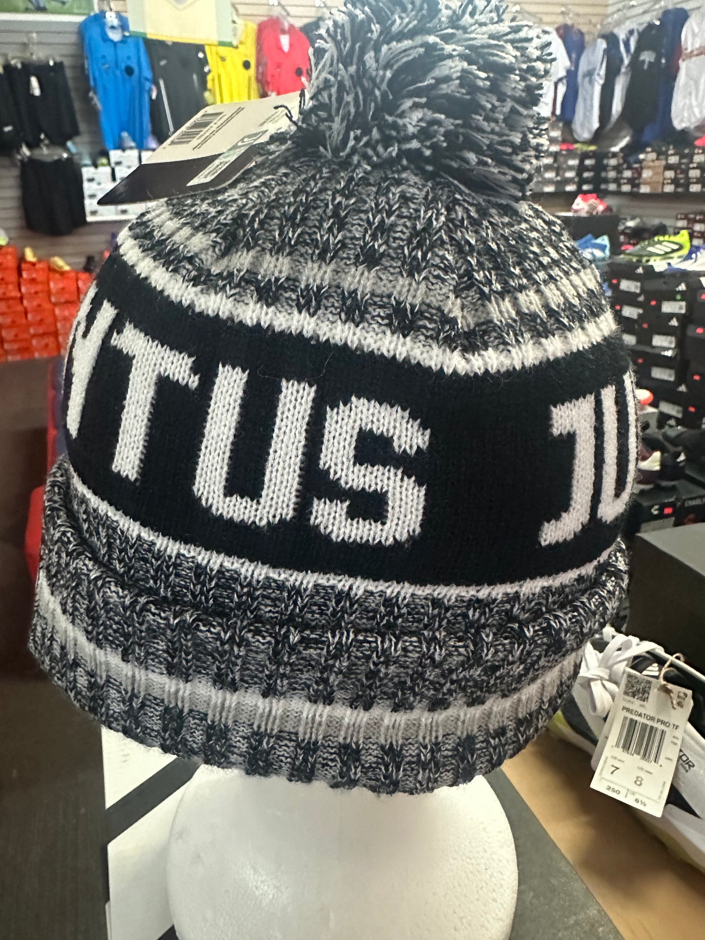 Black and gray knit beanie with 'TUS' text on a mannequin head in a store setting.