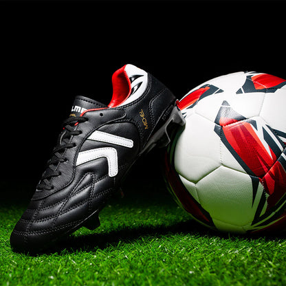 Kelme Black soccer cleat with white accents next to a soccer ball on grass